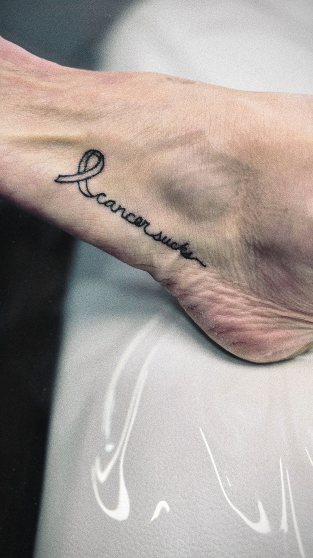 Tiny tattoo by Irene at Lash Box Syosset - delicate cancer awareness script design on foot